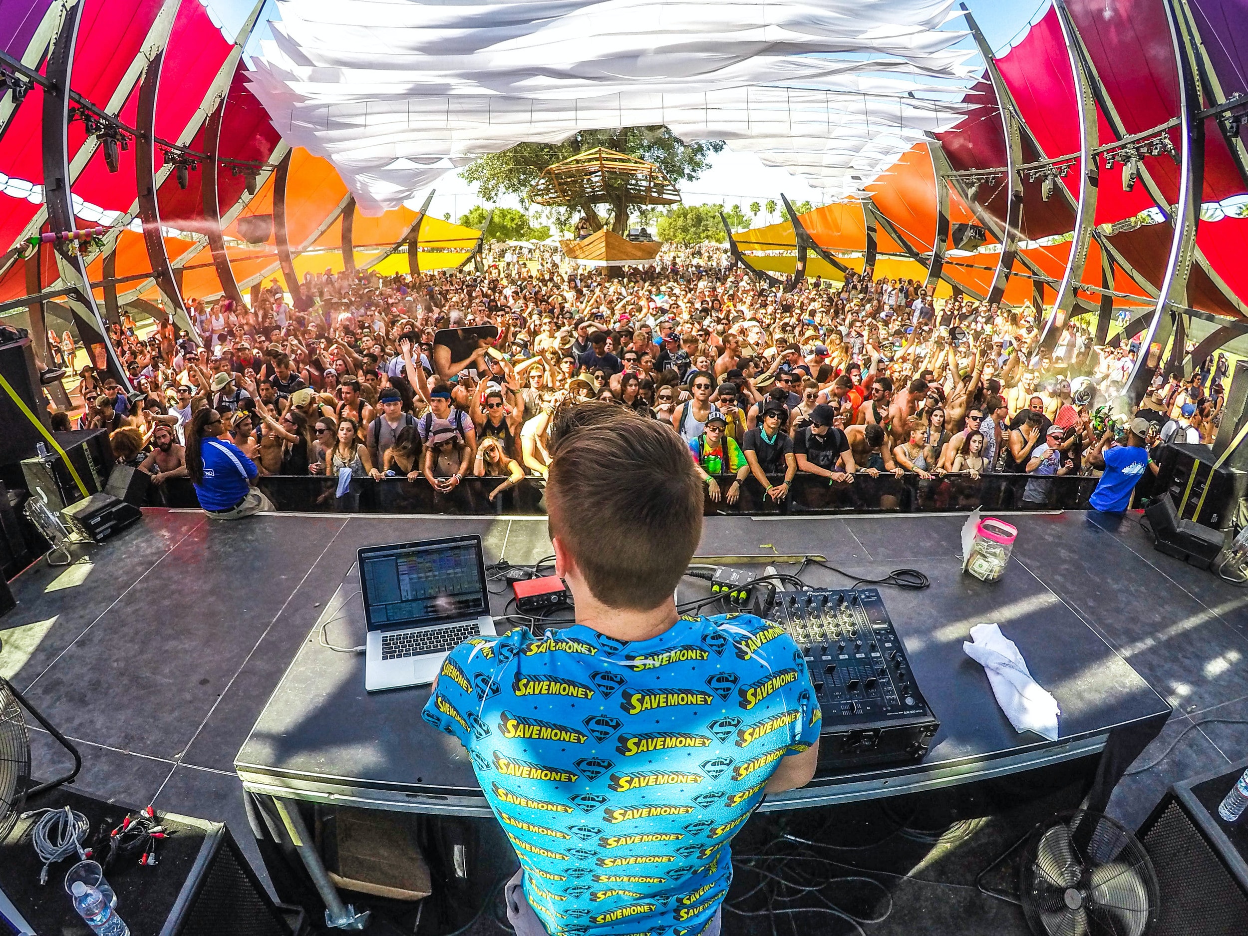 Shows a "behind the DJ decks" view of a music festival.