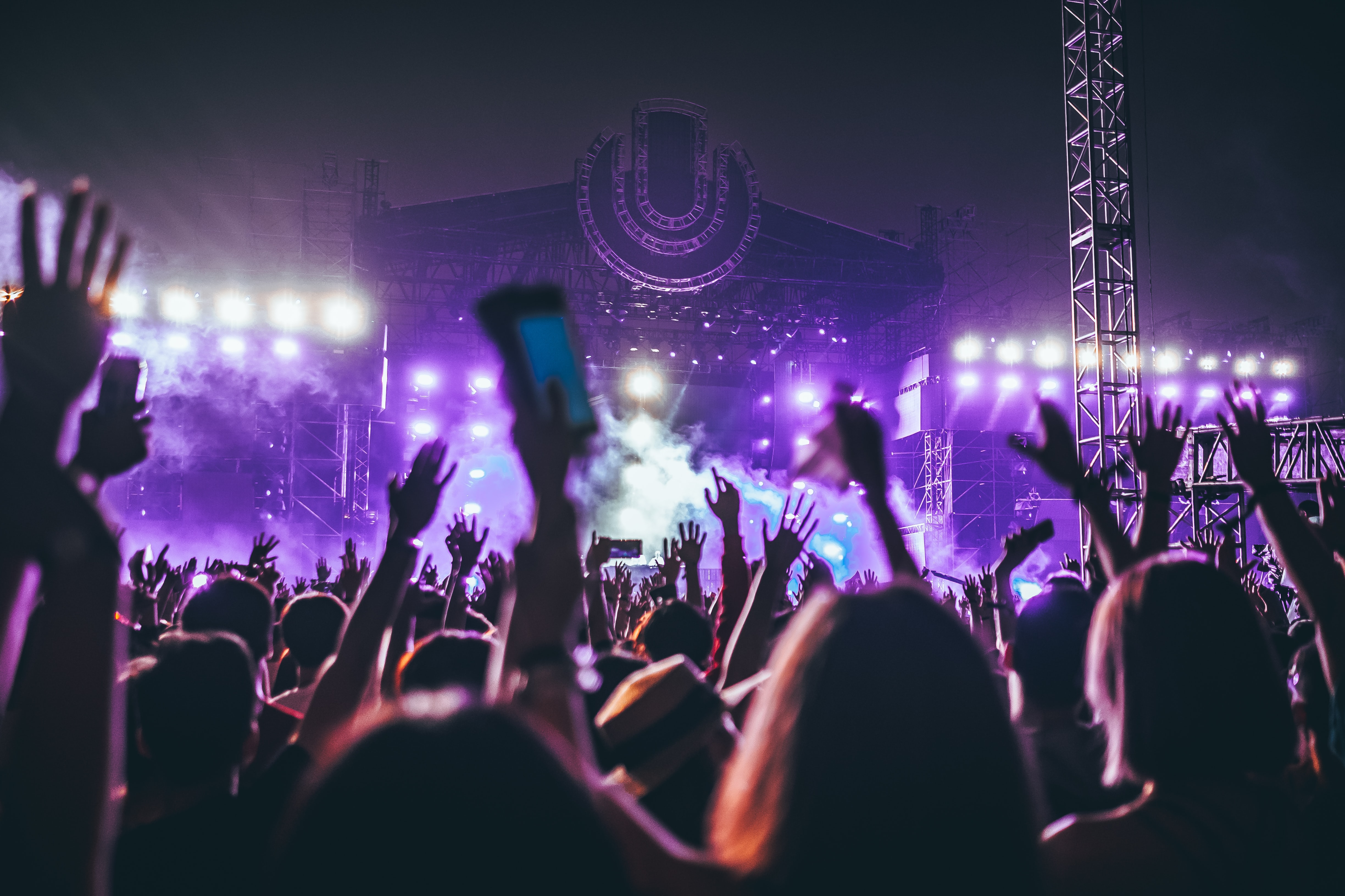 Photo is taken from in the crowd at a music festival with everyone facing towards the main stage with their hands in the air.