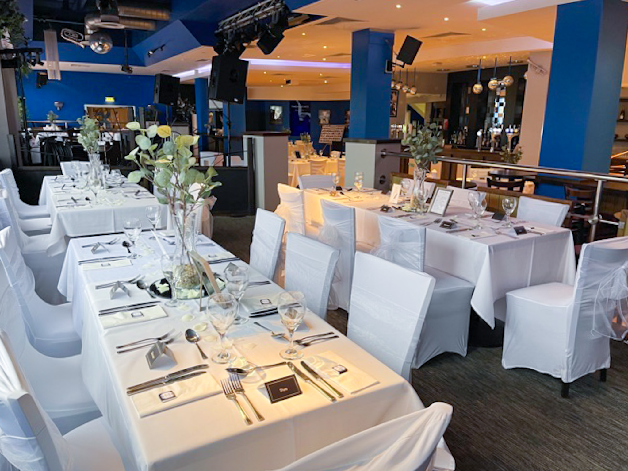 The image shows The Jazz Cafe all dressed up for a wedding with white chair covers and sashes and floral table arrangements.