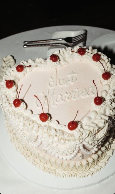 The photo shows a heart-shaped wedding cake with the words "Just Married" in icing on the top. It is decorated with glace cherries round the outside.