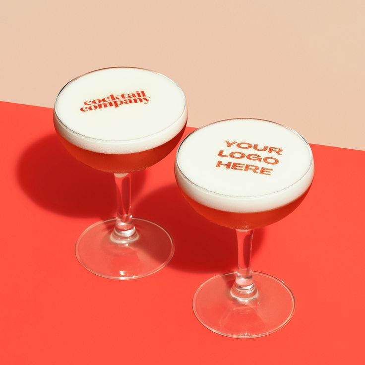 The image shows two red cocktails in coupe glasses. One cocktail reads cocktail company on the top. The second cocktail says your logo here.