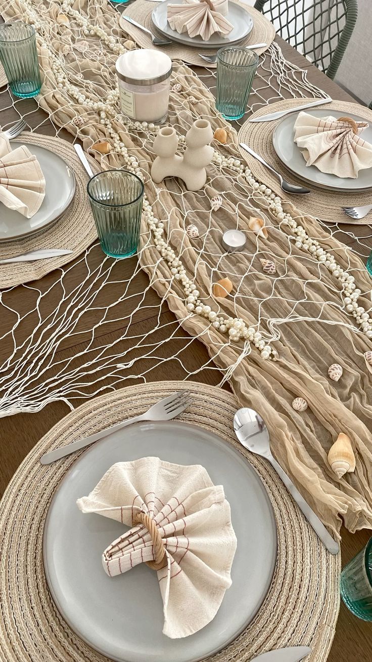 The image shows a table close up of a table laid for dinner. It is themed around the beach and the ocean with shell shaped napkins, shell decorations and netting.