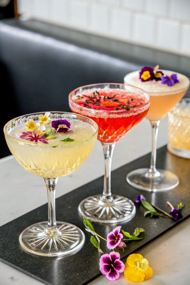 The image shows three different cocktails on a black slate.